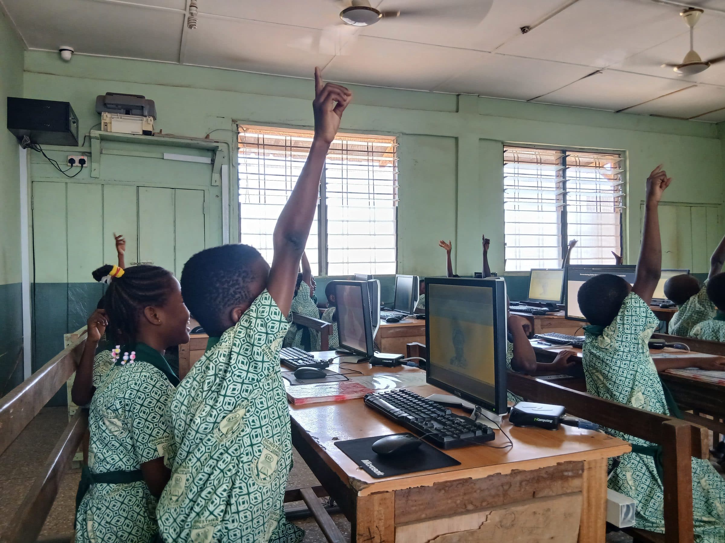 Students raising their hands eagerly in the computer lab